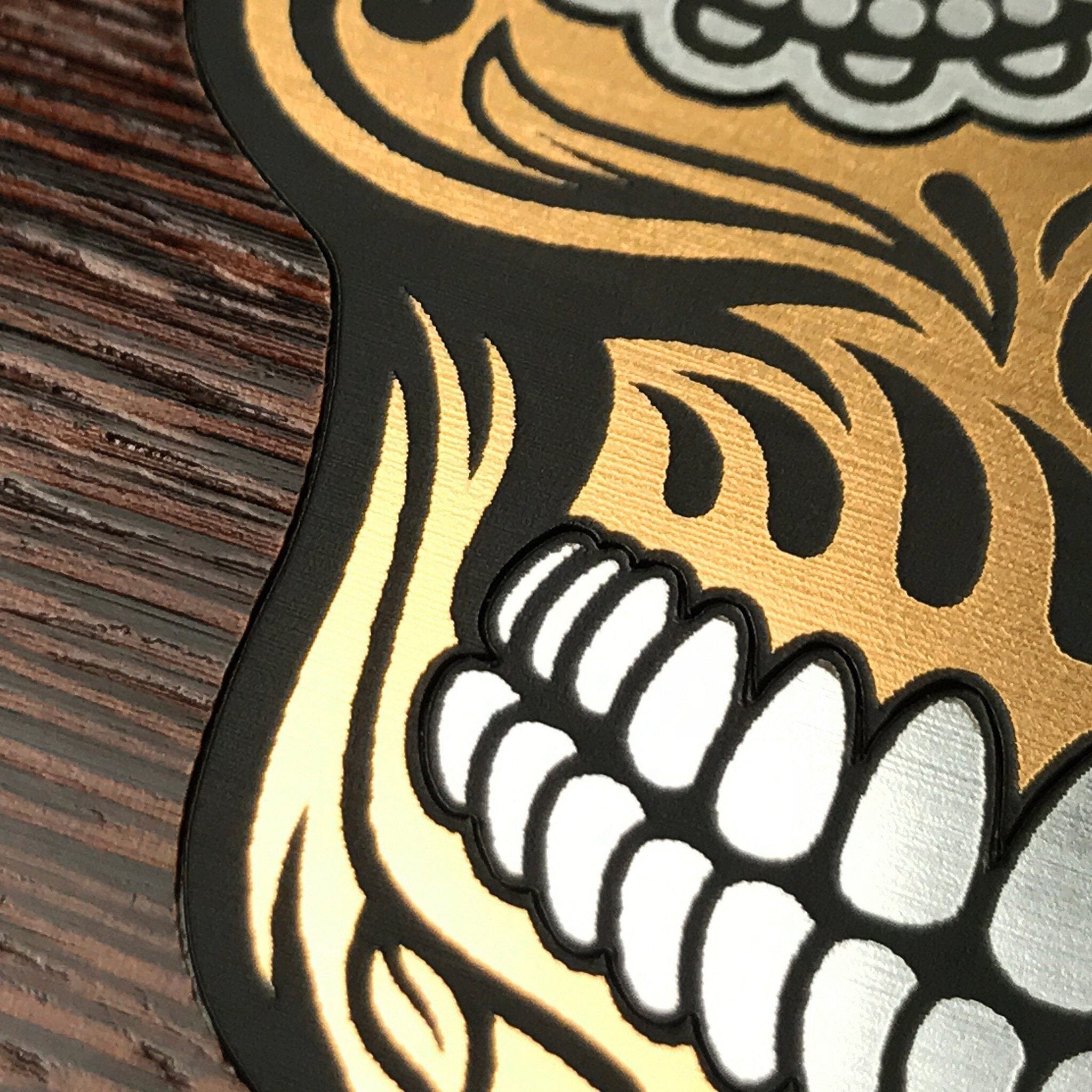 Zoomed in detailed shot of the Calavera Wood Sugar Skull Wood phone case featuring gold and silver engraved metallic inlays