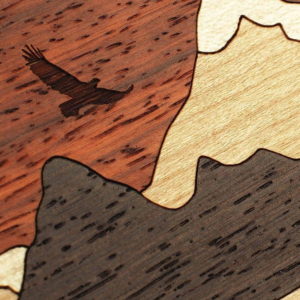 Zoomed in detailed shot of the Cross Country wood phone case by Keyway featuring an eagle engraved in Padauk and mountains cut from Maple, Cherry and Wenge