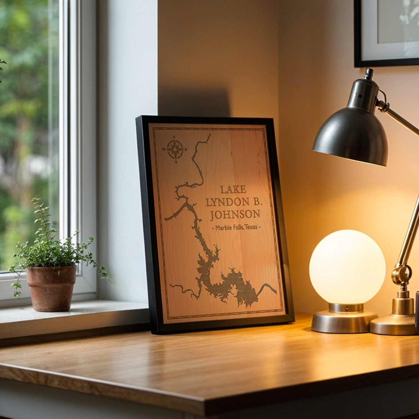 Framed laser-engraved map of Lake Lyndon B. Johnson in Marble Falls, Texas, displayed on a cozy desk by the window. This natural wood wall art adds a warm, rustic touch to home office or study décor.