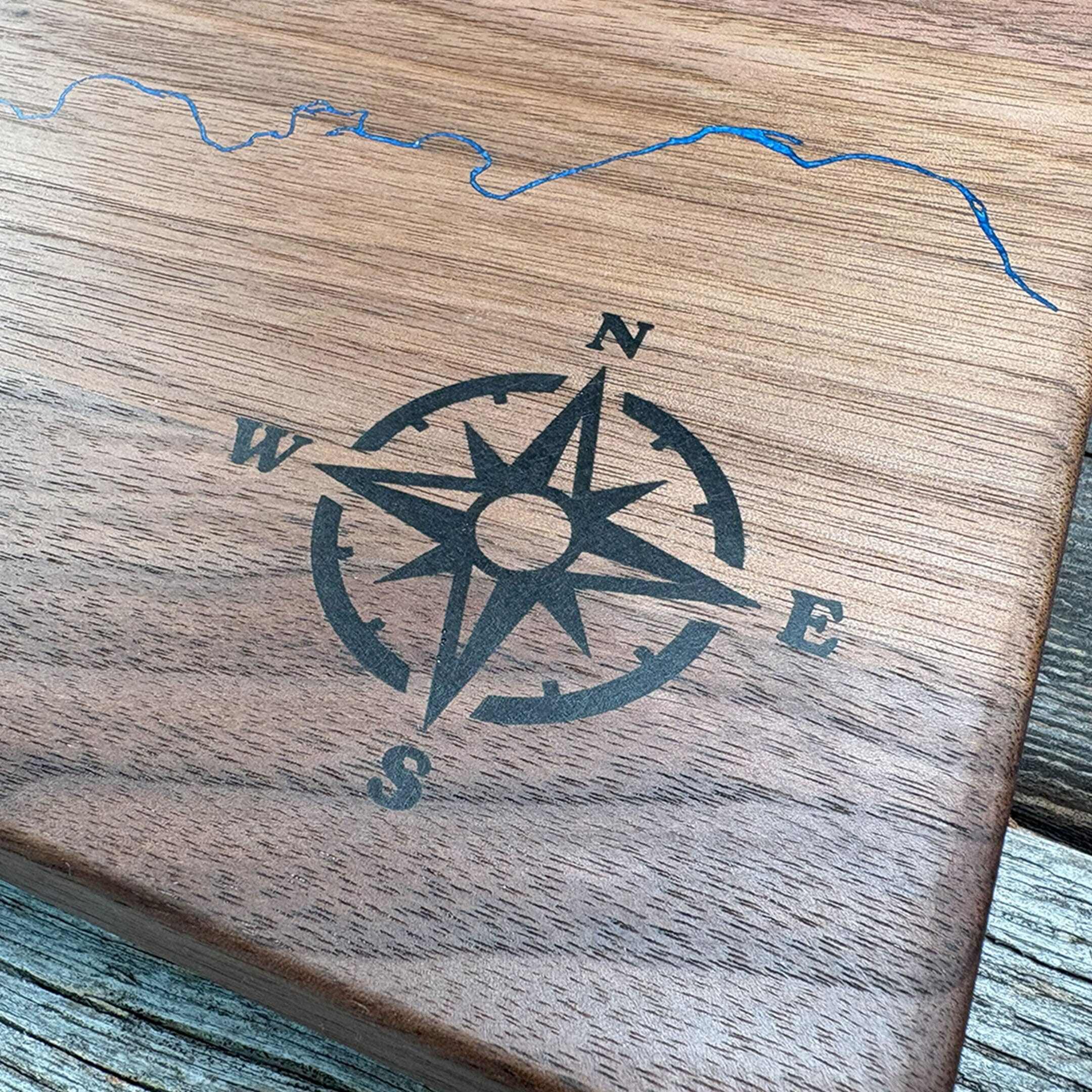 Close-up of custom walnut wood wall art featuring an engraved compass rose design and a blue resin inlay depicting a detailed map, emphasizing craftsmanship and natural wood texture