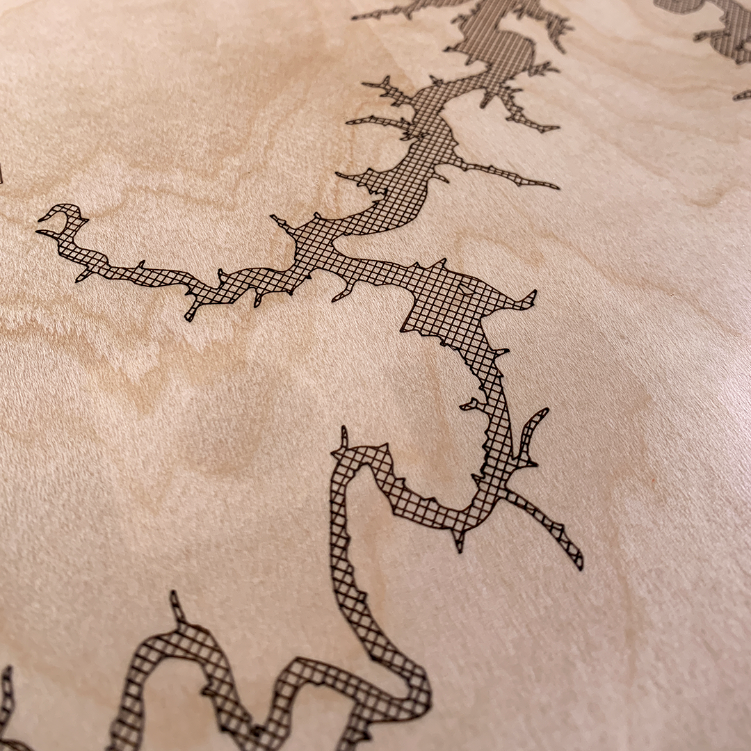 Macro shot of laser-engraved shoreline detail on custom wood lake map. Fine line engraving on natural maple highlights the complexity of water inlets and craftsmanship of the piece.