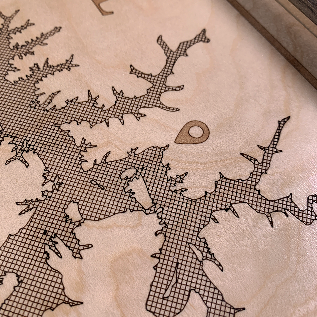 Close-up of laser-engraved point-of-interest marker on detailed wooden map. Fine linework and grid pattern etched on maple wood showcase precision craftsmanship, perfect for custom location wall art.