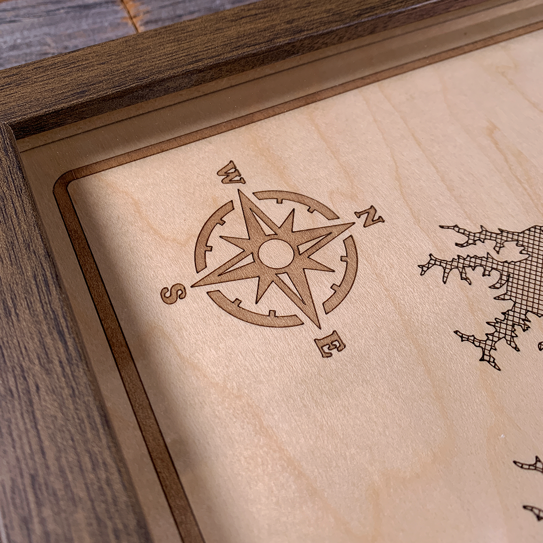 Close-up detail of laser-engraved compass rose on framed wooden lake map. Precision etching on maple wood highlights craftsmanship and nautical design, perfect for rustic and coastal-inspired décor.