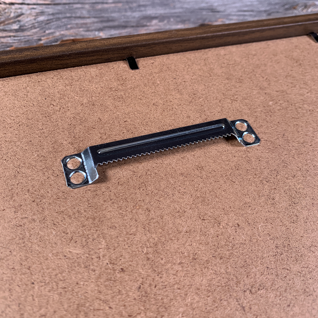 Close-up of metal sawtooth hanger mounted on the back of a framed wooden wall art piece. Durable hardware ensures easy and secure hanging for custom laser-engraved maps or home décor.