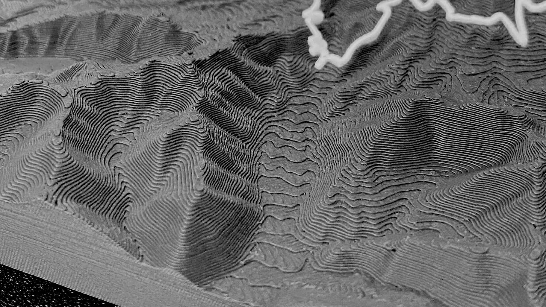 Raking-light macro of a 3D printed terrain relief showing individual 0.2 mm
print layers stacked into sharp ridgelines and gullies, with a white route line
crossing the upper slope and the flat print base visible along the lower edge.